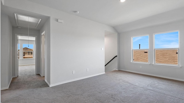 carpeted spare room featuring baseboards, lofted ceiling, and attic access