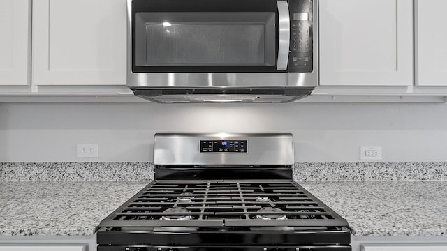 interior details with appliances with stainless steel finishes, white cabinets, and light stone countertops