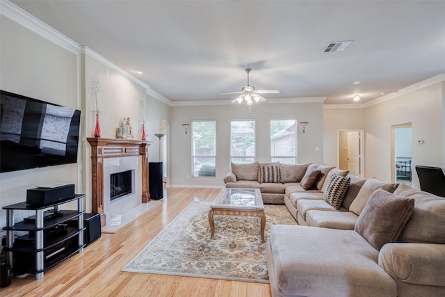 living area featuring crown molding, a premium fireplace, a ceiling fan, wood finished floors, and visible vents