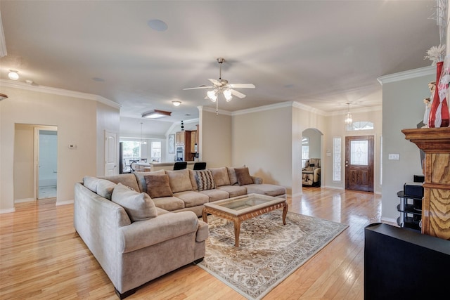 living room with a ceiling fan, ornamental molding, light wood-style floors, baseboards, and arched walkways