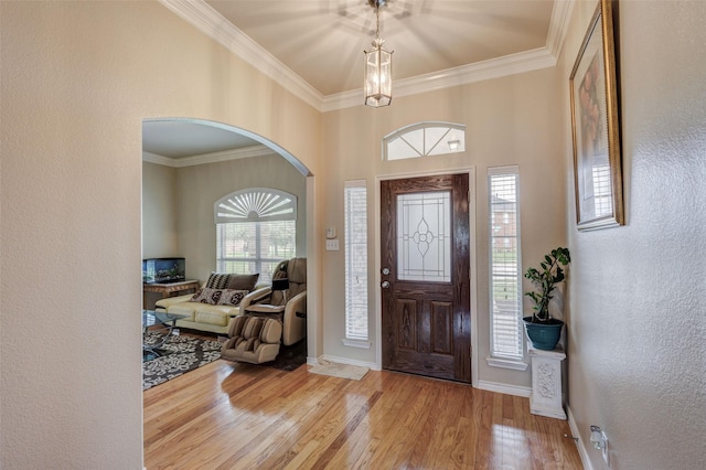 foyer with crown molding, a textured wall, arched walkways, baseboards, and wood finished floors
