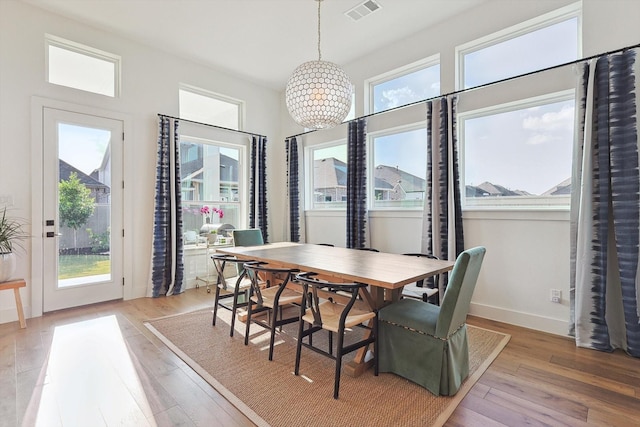 dining space with visible vents, light wood-style flooring, baseboards, and an inviting chandelier