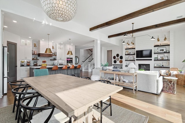 dining area featuring beam ceiling, a large fireplace, wood finished floors, and stairway