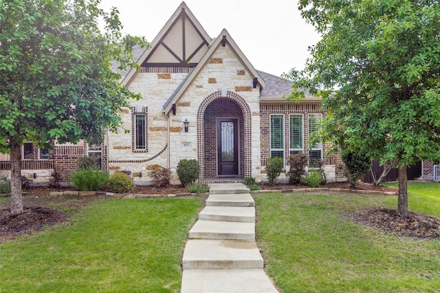 tudor home featuring roof with shingles, stone siding, brick siding, and a front yard