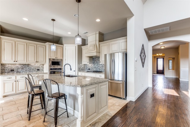 kitchen with arched walkways, cream cabinetry, a sink, light wood-style flooring, and stainless steel appliances