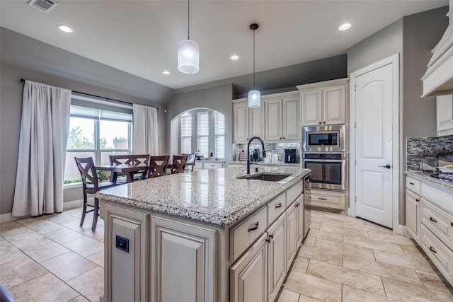 kitchen with backsplash, visible vents, a center island with sink, a sink, and stainless steel appliances
