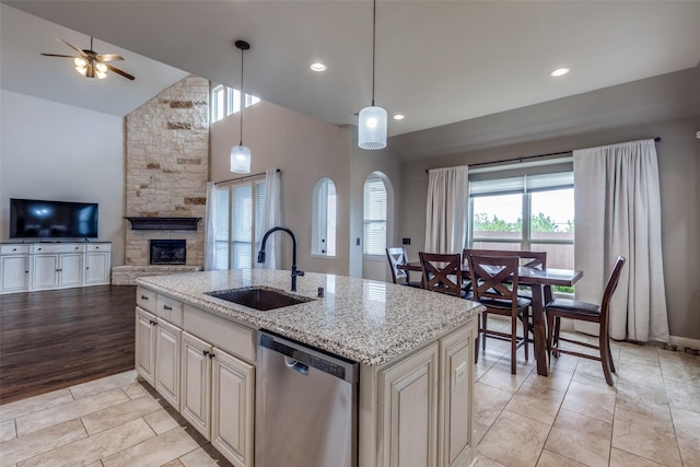 kitchen with open floor plan, ceiling fan, light stone counters, a sink, and dishwasher