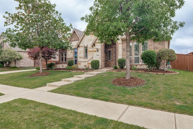 view of front facade with fence, brick siding, a front lawn, and stone siding