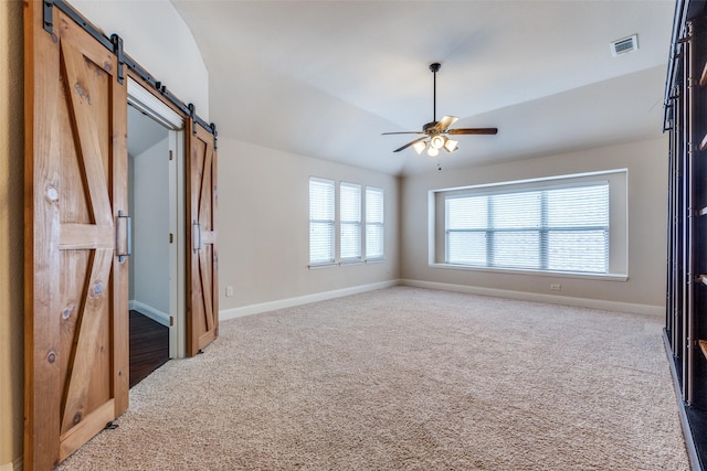 spare room with a barn door, light carpet, a ceiling fan, baseboards, and visible vents