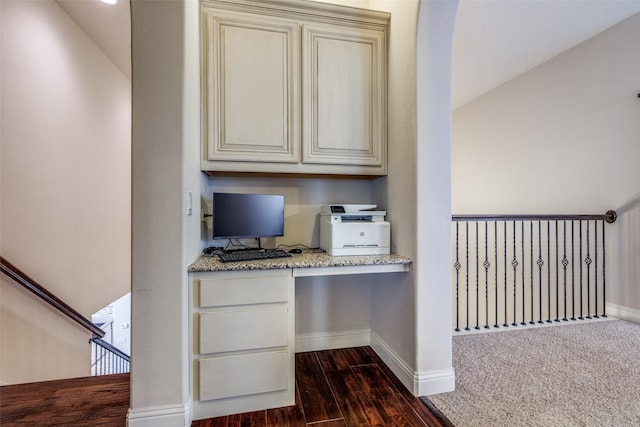 interior space with baseboards, dark wood finished floors, built in desk, and cream cabinetry