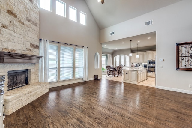 living area with high vaulted ceiling, visible vents, a stone fireplace, and light wood-style floors