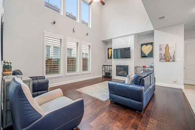 living area with a fireplace, baseboards, wood finished floors, a towering ceiling, and visible vents