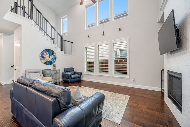 living room featuring a high ceiling, a fireplace, dark wood finished floors, a ceiling fan, and stairway