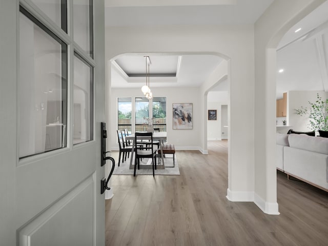 foyer entrance with a raised ceiling, baseboards, arched walkways, and light wood-style flooring