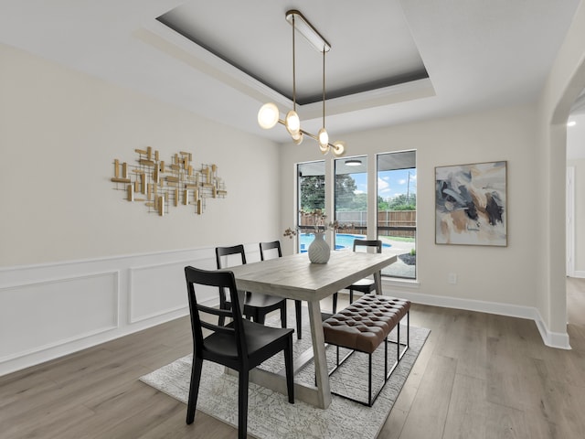 dining area featuring an inviting chandelier, arched walkways, a tray ceiling, and wood finished floors