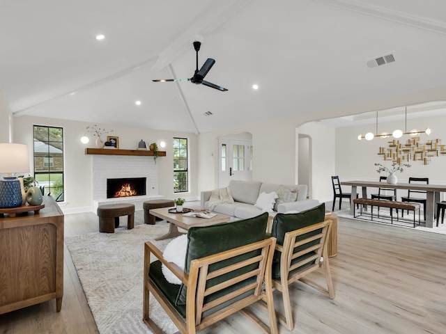 living room featuring a fireplace, light wood-style floors, ceiling fan with notable chandelier, a wealth of natural light, and visible vents