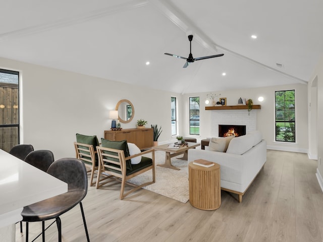 living area with vaulted ceiling with beams, plenty of natural light, a brick fireplace, and light wood finished floors