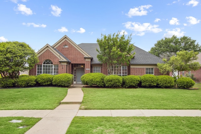 view of front of home with roof with shingles, a front yard, and brick siding