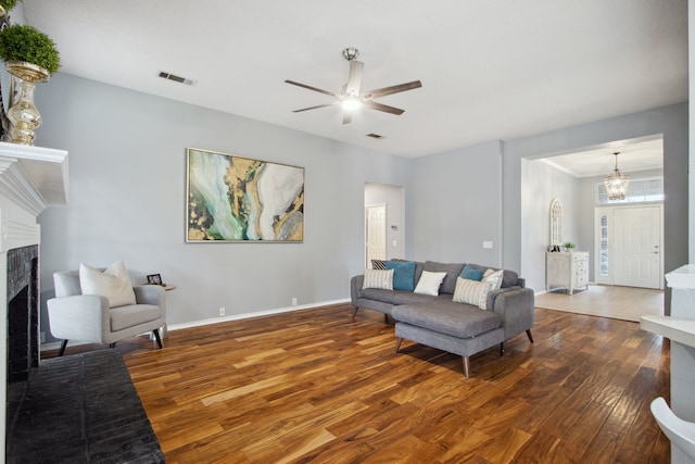 living area with visible vents, a fireplace, wood finished floors, baseboards, and ceiling fan with notable chandelier
