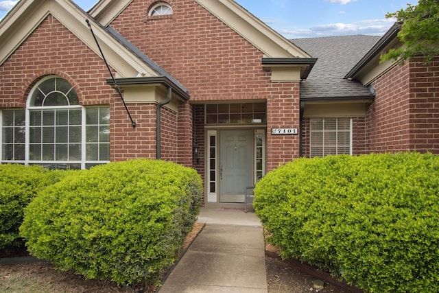 entrance to property with brick siding and a shingled roof