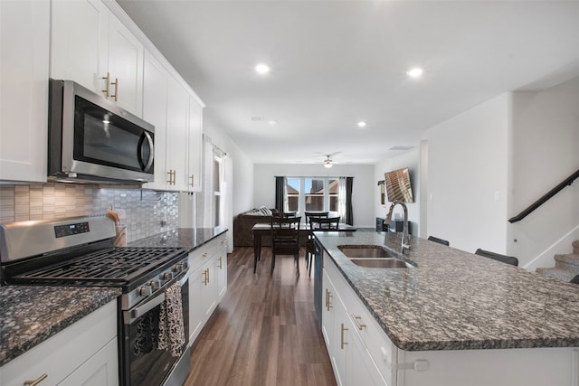 kitchen featuring backsplash, a center island with sink, a sink, dark wood-style floors, and stainless steel appliances