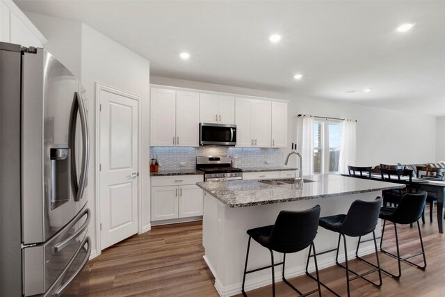kitchen with a kitchen breakfast bar, tasteful backsplash, light stone counters, a sink, and appliances with stainless steel finishes