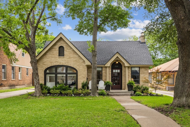 tudor home with brick siding, a front lawn, and roof with shingles