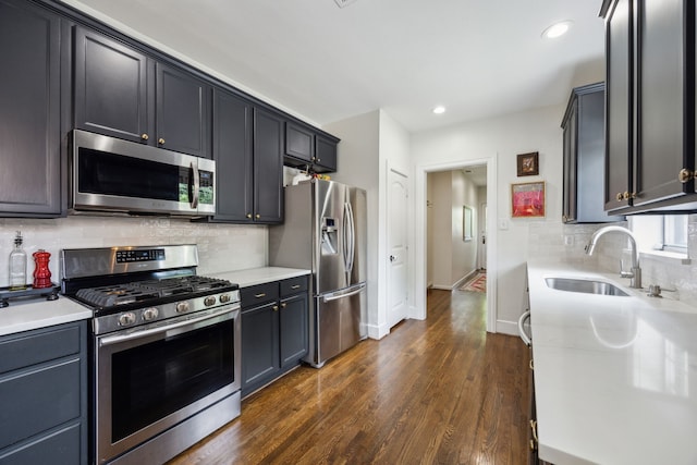 kitchen with dark wood-style flooring, appliances with stainless steel finishes, a sink, light countertops, and backsplash