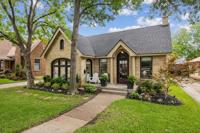 tudor home featuring roof with shingles, a front lawn, and brick siding