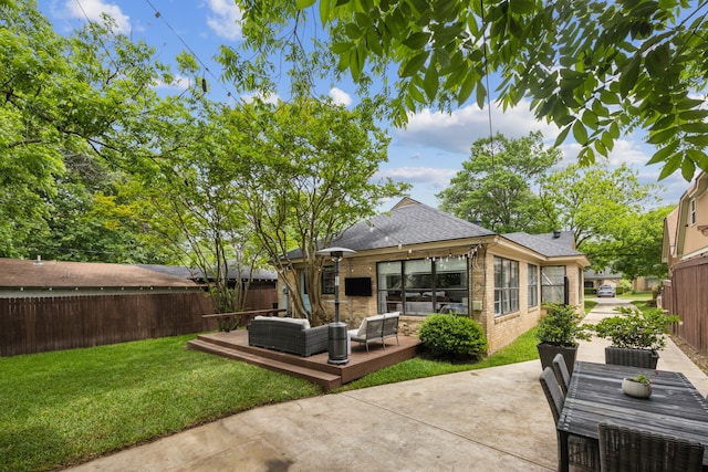 rear view of house featuring a deck, a fenced backyard, roof with shingles, brick siding, and a lawn
