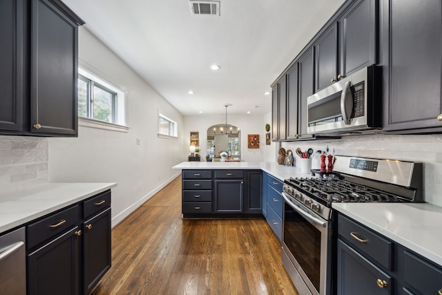 kitchen with visible vents, dark wood-style flooring, a peninsula, backsplash, and stainless steel appliances