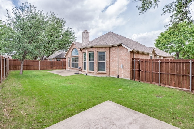rear view of property with a fenced backyard, a chimney, brick siding, a patio area, and a yard