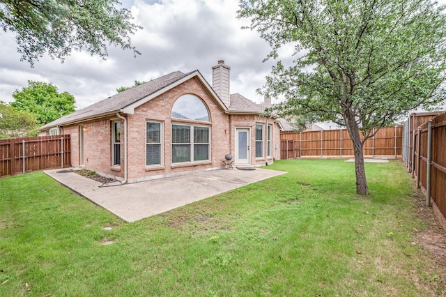 rear view of property with a chimney, a patio area, brick siding, a fenced backyard, and a yard