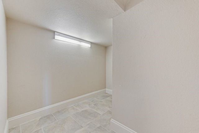 basement featuring light tile patterned floors, a textured ceiling, and baseboards