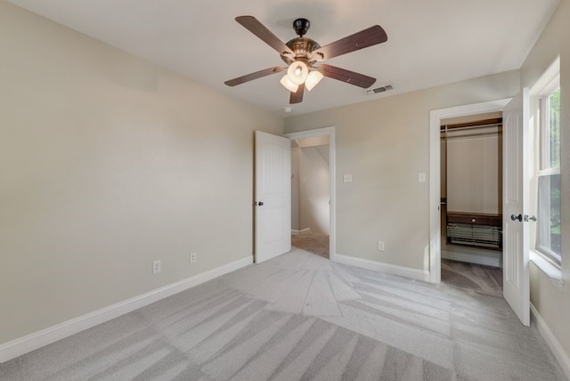 unfurnished bedroom with a walk in closet, baseboards, light colored carpet, and visible vents