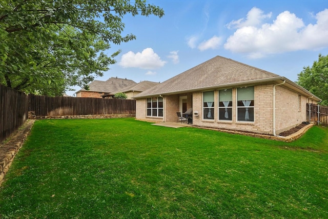 rear view of property with a shingled roof, brick siding, a fenced backyard, a lawn, and a patio