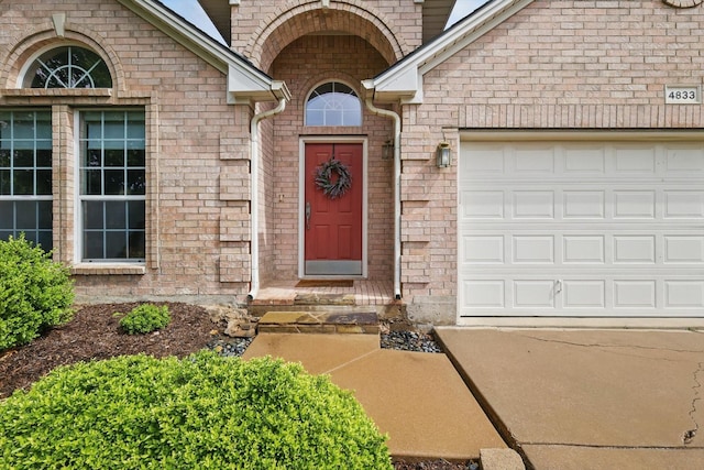 doorway to property featuring brick siding, an attached garage, and driveway