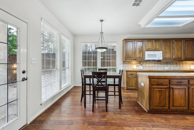 kitchen featuring brown cabinetry, decorative backsplash, white microwave, visible vents, and dark wood-style floors