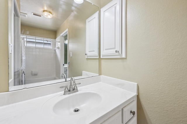 full bathroom with vanity, a textured wall, and visible vents