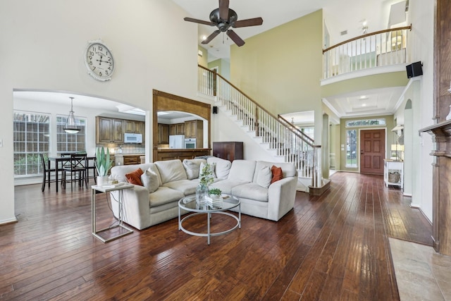 living area featuring stairs, ceiling fan, hardwood / wood-style floors, and a towering ceiling