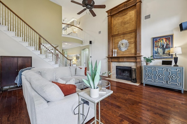 living area with a high ceiling, a fireplace, stairs, a ceiling fan, and wood finished floors