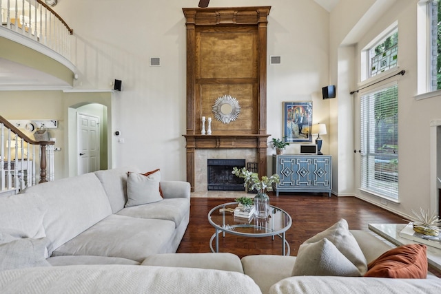 living room with visible vents, a towering ceiling, wood finished floors, arched walkways, and a premium fireplace