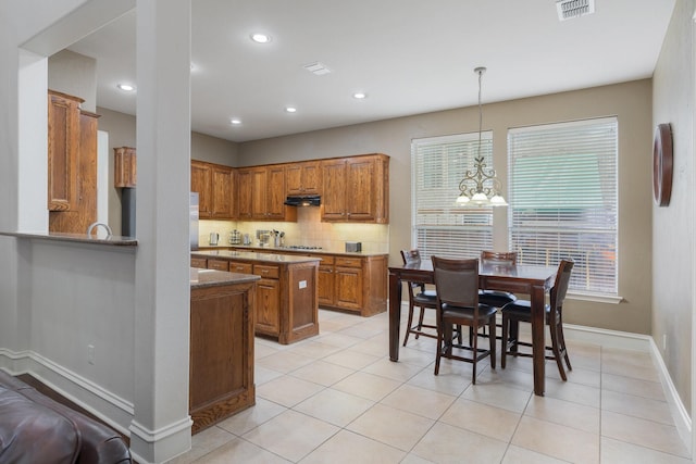 kitchen featuring decorative backsplash, brown cabinetry, visible vents, light tile patterned floors, and under cabinet range hood
