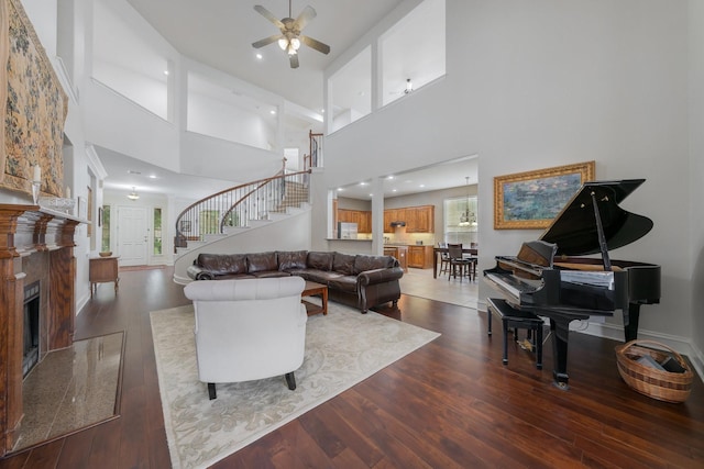 living area with ceiling fan, dark wood finished floors, stairway, and a towering ceiling