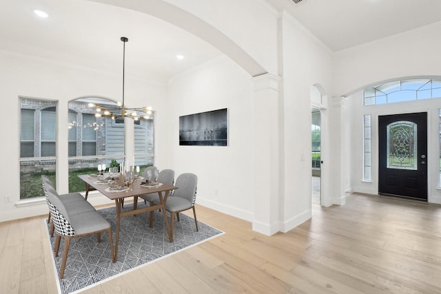 dining space with arched walkways, a chandelier, baseboards, wood finished floors, and ornamental molding
