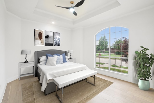 bedroom featuring a tray ceiling, ornamental molding, ceiling fan, and light wood finished floors