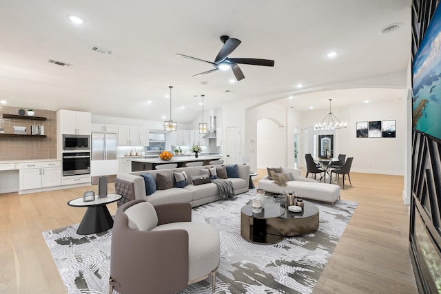 living area with arched walkways, visible vents, light wood-style flooring, and ceiling fan with notable chandelier
