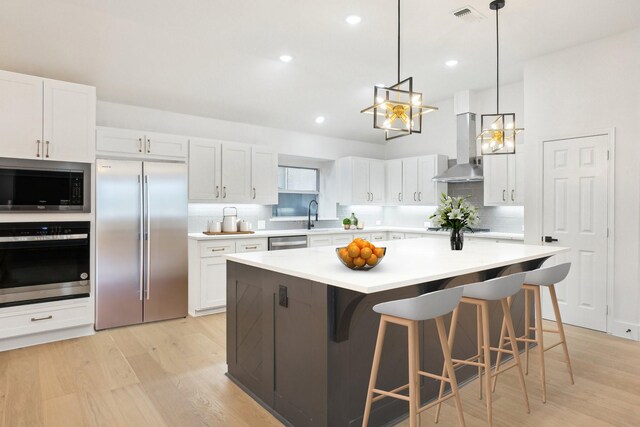 kitchen featuring wall chimney range hood, built in appliances, light countertops, and visible vents