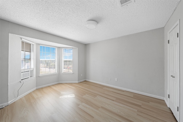 empty room featuring a textured ceiling, visible vents, baseboards, and light wood-style floors