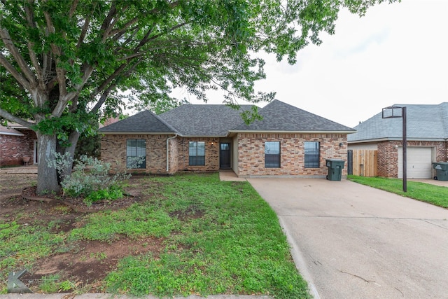 ranch-style house featuring fence, a shingled roof, brick siding, a front yard, and concrete driveway
